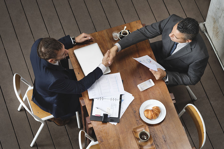 Business Insurance - View from Above of Two Businessmen Sitting Around a Wooden Table Shaking Hands During a Business Meeting