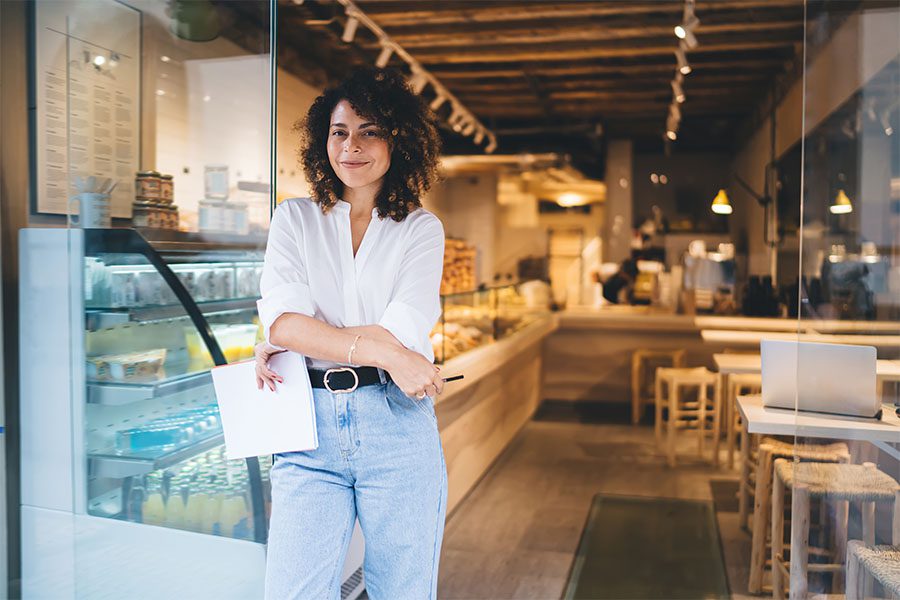 Contact - Portrait of a Young Small Business Woman Standing Outside Her Cafe With Her Arms Crossed While Holding a Piece of Paper